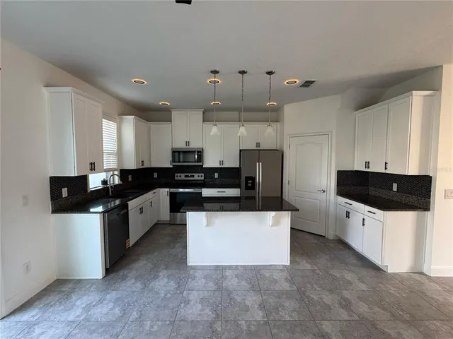 a large kitchen with stainless steel appliances a sink a stove a refrigerator a center island and a window