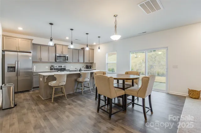 a kitchen with kitchen island a dining table chairs stainless steel appliances and cabinets