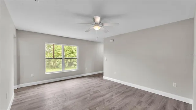 an empty room with wooden floor ceiling fan and windows