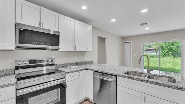 a kitchen with granite countertop white cabinets appliances and a window