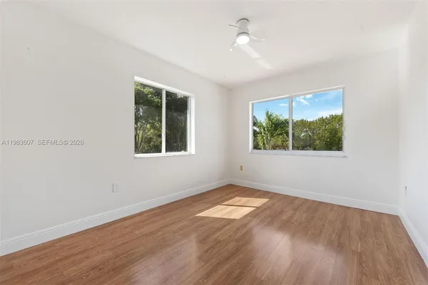 an empty room with wooden floor ceiling fan and windows