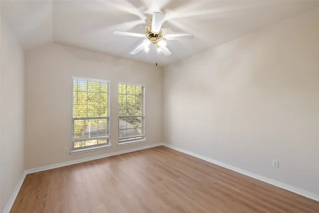 an empty room with wooden floor fan and windows