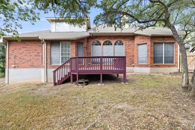 a view of a brick house with a small yard and a large tree