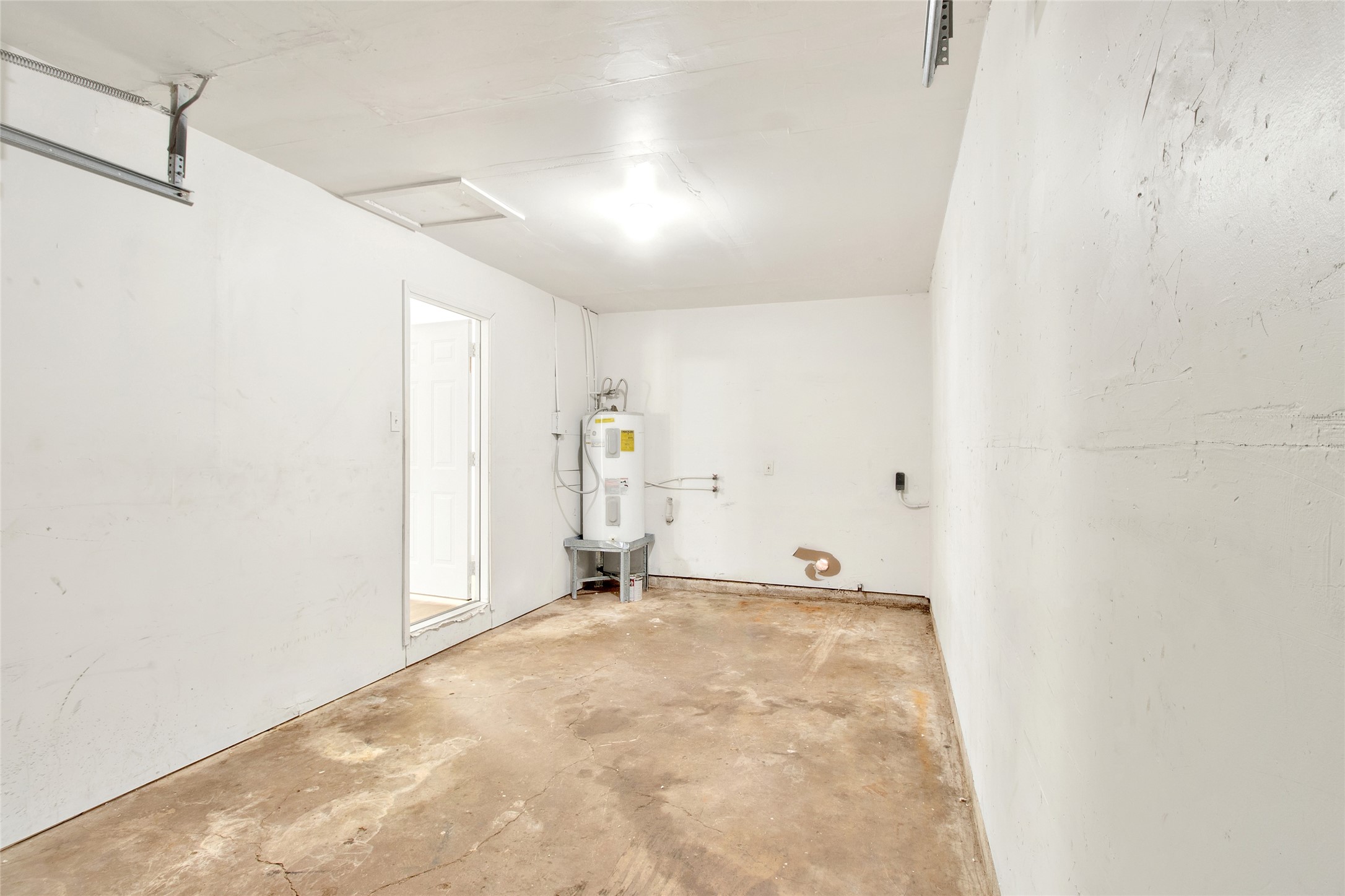 506 Edgebrook Drive Houston, TX 77034 - Photo 16 of 18 This photo shows a spacious one car garage, utility room, water heater, concrete floor, and white walls. It's well-lit and has potential for storage or a workshop area.