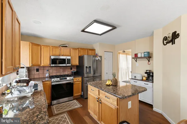 a kitchen with stainless steel appliances granite countertop a stove top oven a sink dishwasher and a refrigerator with wooden floor