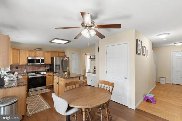 a kitchen with stainless steel appliances granite countertop a stove a refrigerator a kitchen island a dining table and chairs with wooden floor