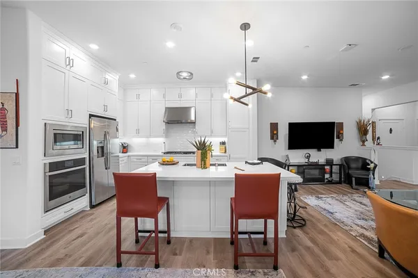 a living room with stainless steel appliances furniture a flat screen tv and kitchen view