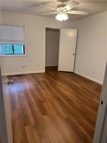an empty room with wooden floor chandelier fan and windows