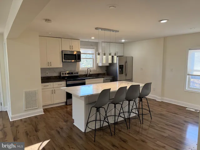 a kitchen with stainless steel appliances kitchen island granite countertop a stove a sink a microwave a dining table and chairs with wooden floor