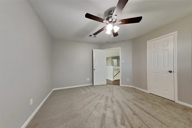 a view of an empty room with wooden floor and a ceiling fan