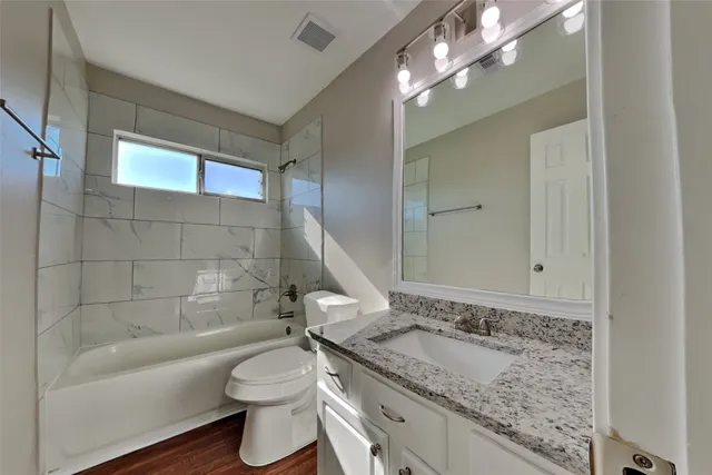 a bathroom with a granite countertop sink a toilet a mirror and bathtub