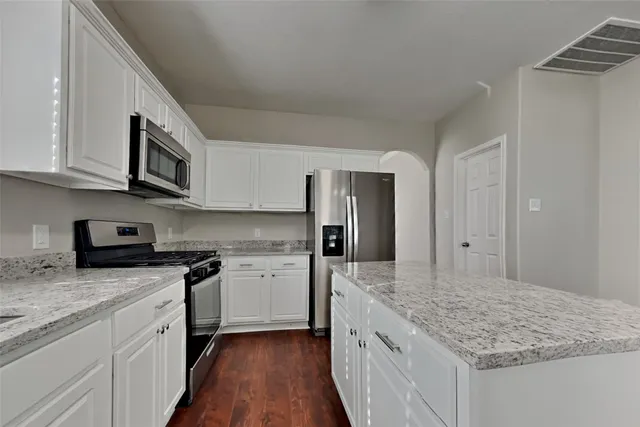 a kitchen with stainless steel appliances granite countertop a stove top oven a refrigerator a sink and dishwasher with wooden floor