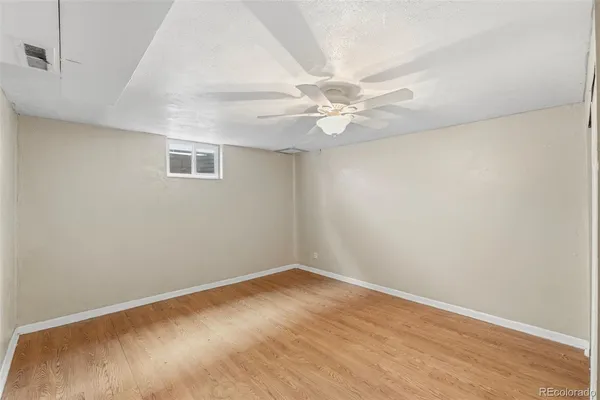 an empty room with a chandelier fan and wooden floor