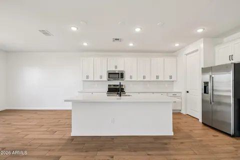 a large kitchen with stainless steel appliances granite countertop a stove a sink a refrigerator and white cabinets with wooden floor