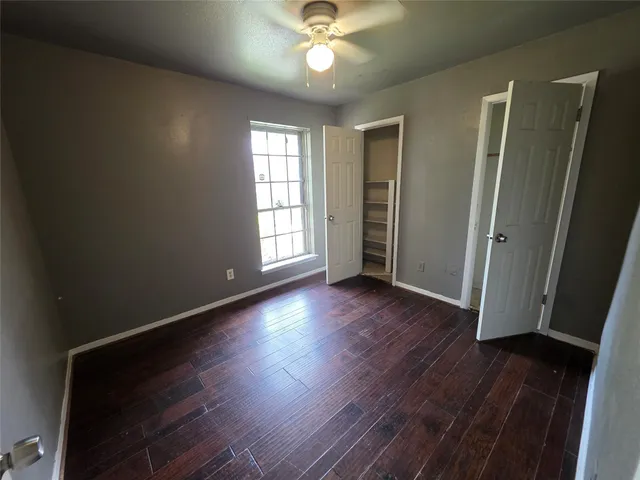 an empty room with wooden floor chandelier fan and windows