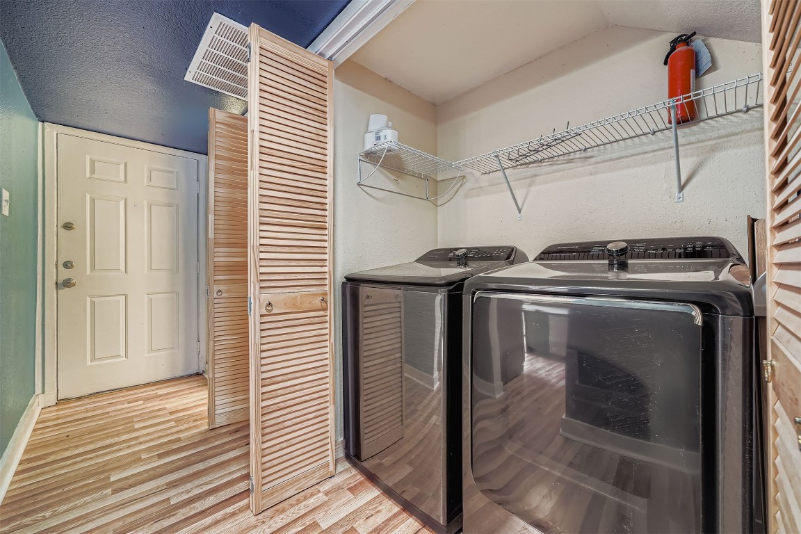 2018 West Rundberg Lane, Unit 2B Austin, TX 78758 - Photo 15 of 31 Compact laundry area with modern black washer and dryer units. It features wood-style flooring, louvered doors, and shelving above the appliances for storage. The area is adjacent to the hallway and adjacent to the kitchen.