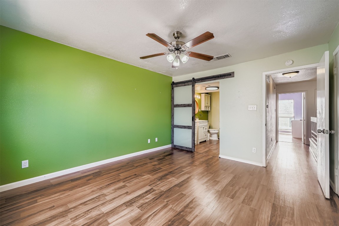 2018 West Rundberg Lane, Unit 2B Austin, TX 78758 - Photo 18 of 31 Unfurnished bedroom featuring a barn door, wood finished floors, ceiling fan, ensuite bathroom, and a textured ceiling