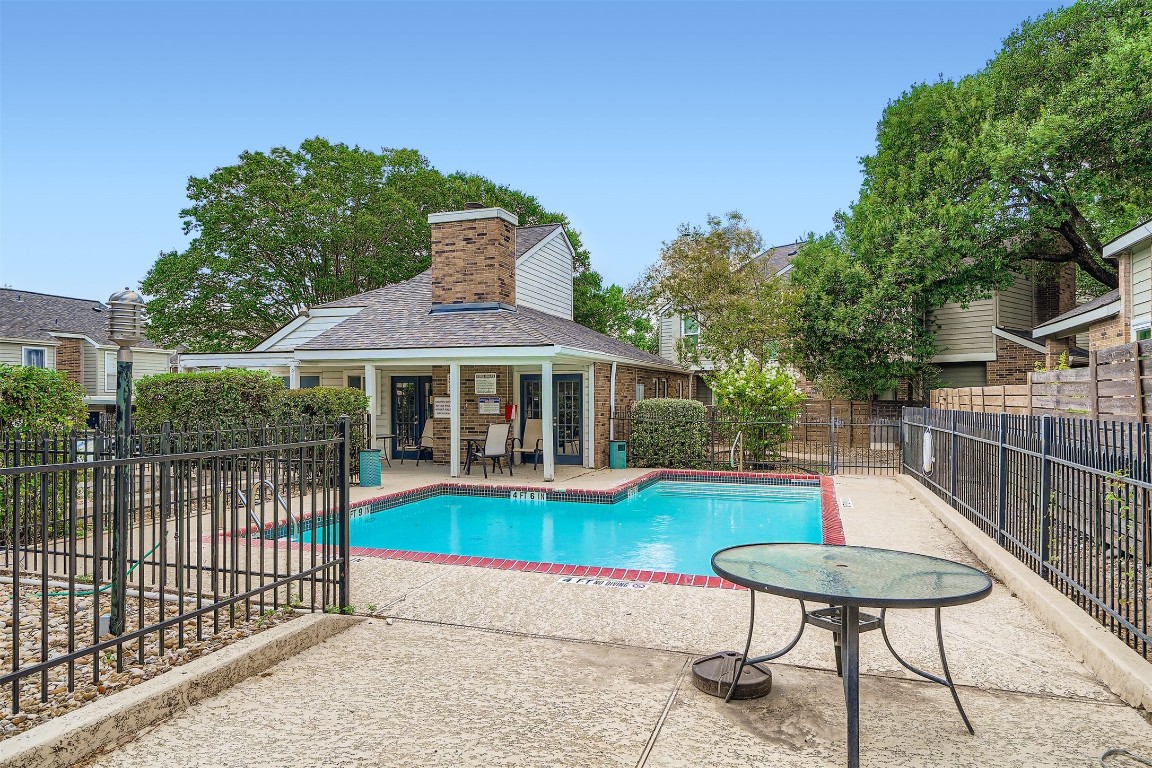 2018 West Rundberg Lane, Unit 2B Austin, TX 78758 - Photo 4 of 31 Community outdoor pool, surrounded by a secure fence. The area includes a cozy patio with a brick structure, lush greenery, and ample seating, perfect for relaxation or entertaining.