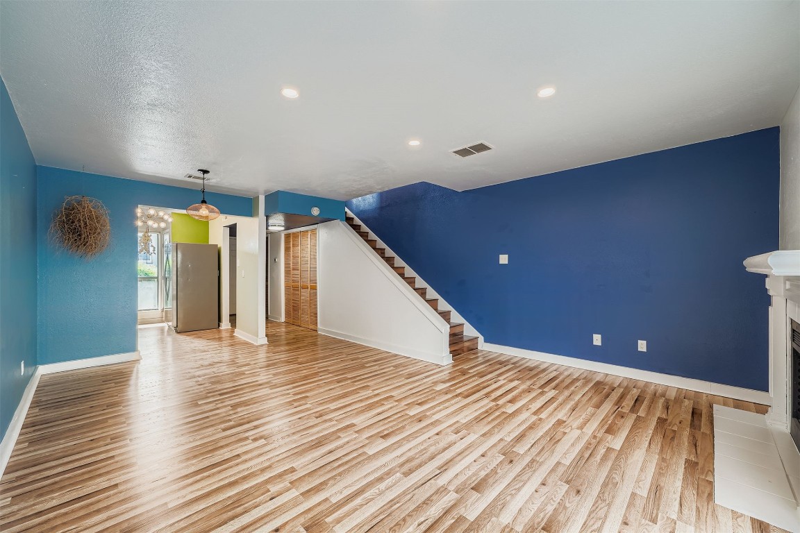 2018 West Rundberg Lane, Unit 2B Austin, TX 78758 - Photo 7 of 31 Spacious, open-concept living area with modern wood flooring and vibrant blue accent walls. Features include recessed lighting, a cozy corner fireplace, and a staircase leading to the upper level. The adjacent dining area has a stylish light fixture and direct access to the kitchen.