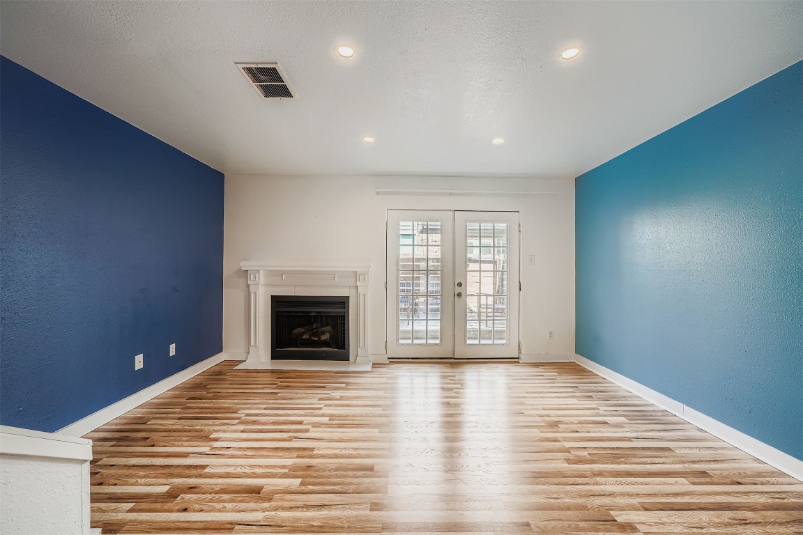 2018 West Rundberg Lane, Unit 2B Austin, TX 78758 - Photo 10 of 31 Unfurnished living room with a textured wall, french doors, light wood-type flooring, a fireplace with flush hearth, and recessed lighting