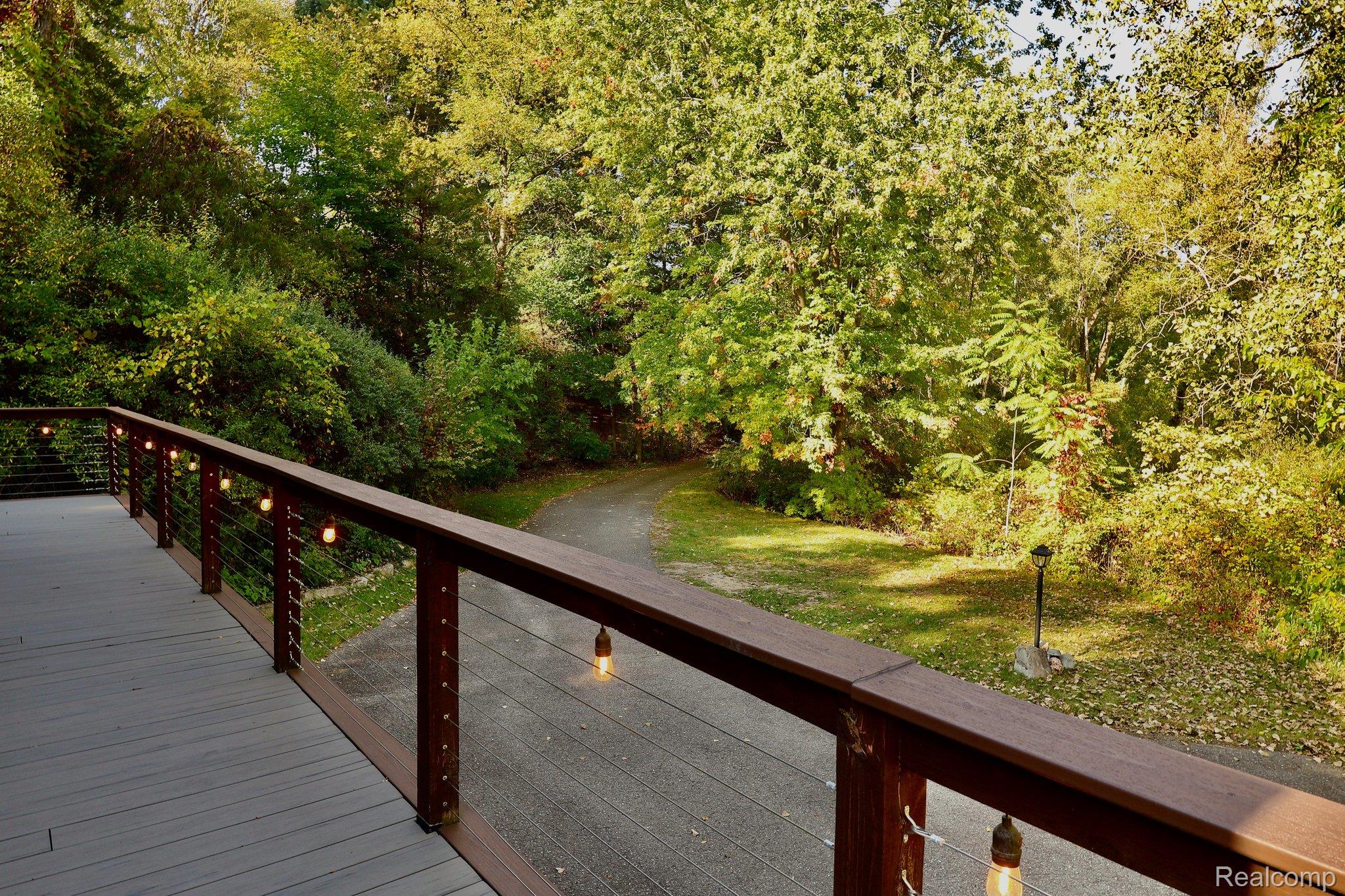 8312 Whitmore Lake Road Brighton, MI 48116 - Photo 18 of 43 Deck with cable railing and strung lighting, overlooking a natural landscape with a paved pathway