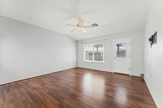 an empty room with wooden floor ceiling fan and windows