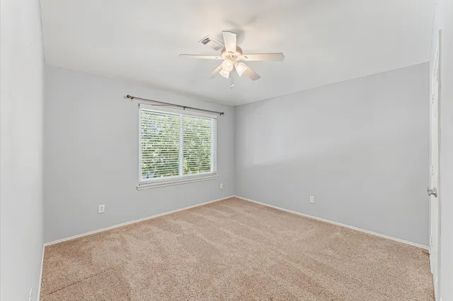 an empty room with chandelier fan and windows