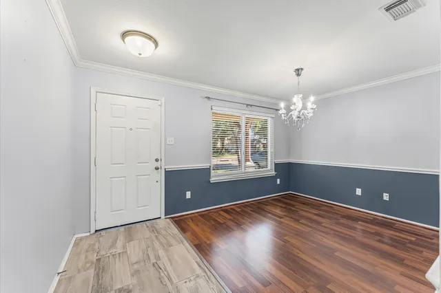 an empty room with wooden floor chandelier and windows