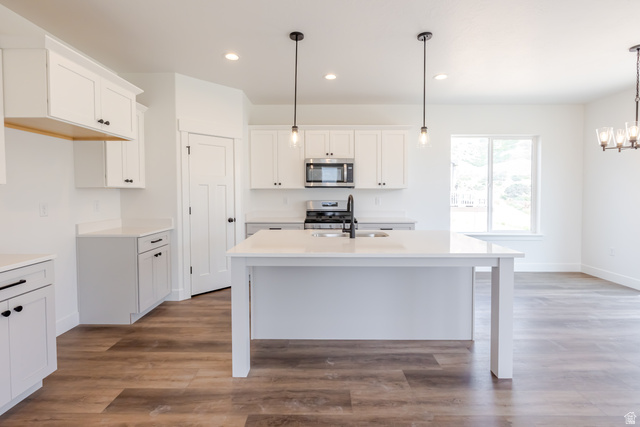 195 West Harmony Rdg Parkway, Unit 601 Mapleton, UT 84664 - Photo 5 of 23 Bright kitchen featuring white cabinetry, a central island with a sink and matte black faucet, stainless steel microwave, and wood-finish flooring