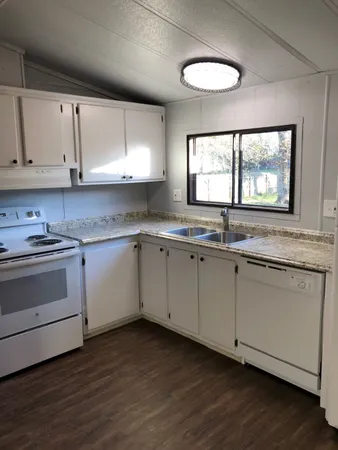 a kitchen with granite countertop white cabinets white appliances a sink and a window