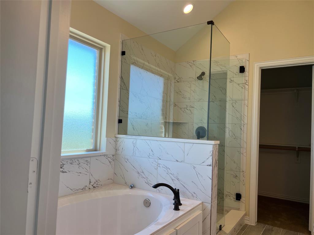 8008 County Road 1058 Rice, TX 75155 - Photo 15 of 25 Modern bathroom featuring a built-in tub with matte black fixtures, a walk-in shower with glass enclosure and marble-look tile, and a frosted privacy window