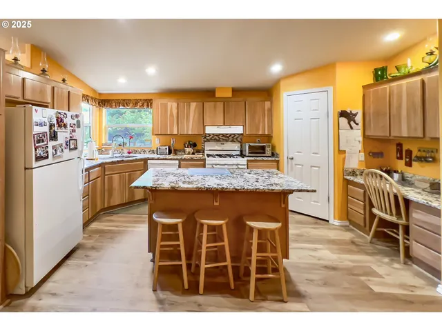 a kitchen with stainless steel appliances kitchen island granite countertop a refrigerator a stove a sink a dining table and chairs with wooden floor