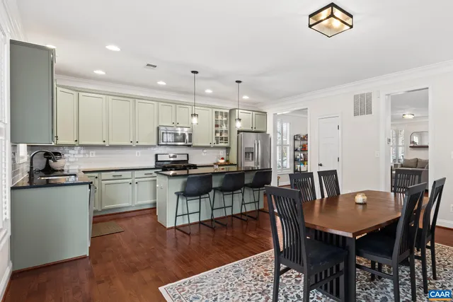 a kitchen with stainless steel appliances granite countertop a stove a refrigerator a kitchen island a dining table and chairs with wooden floor