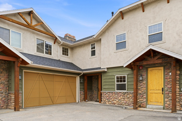 3634 North Huntsman Path, Unit C203 Eden, UT 84310 - Photo 2 of 27 Exterior featuring stucco and river stone accents, a prominent garage with a wood-finish door, and a covered entry with a distinctive yellow front door