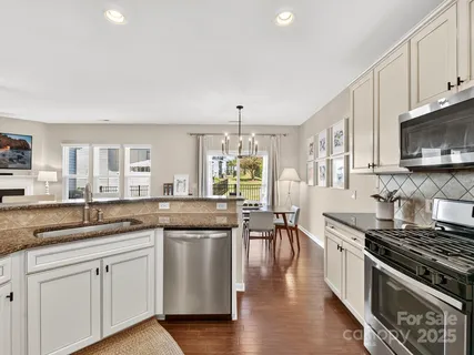 a kitchen with stainless steel appliances granite countertop a stove top oven a sink dishwasher a dining table and chairs with wooden floor