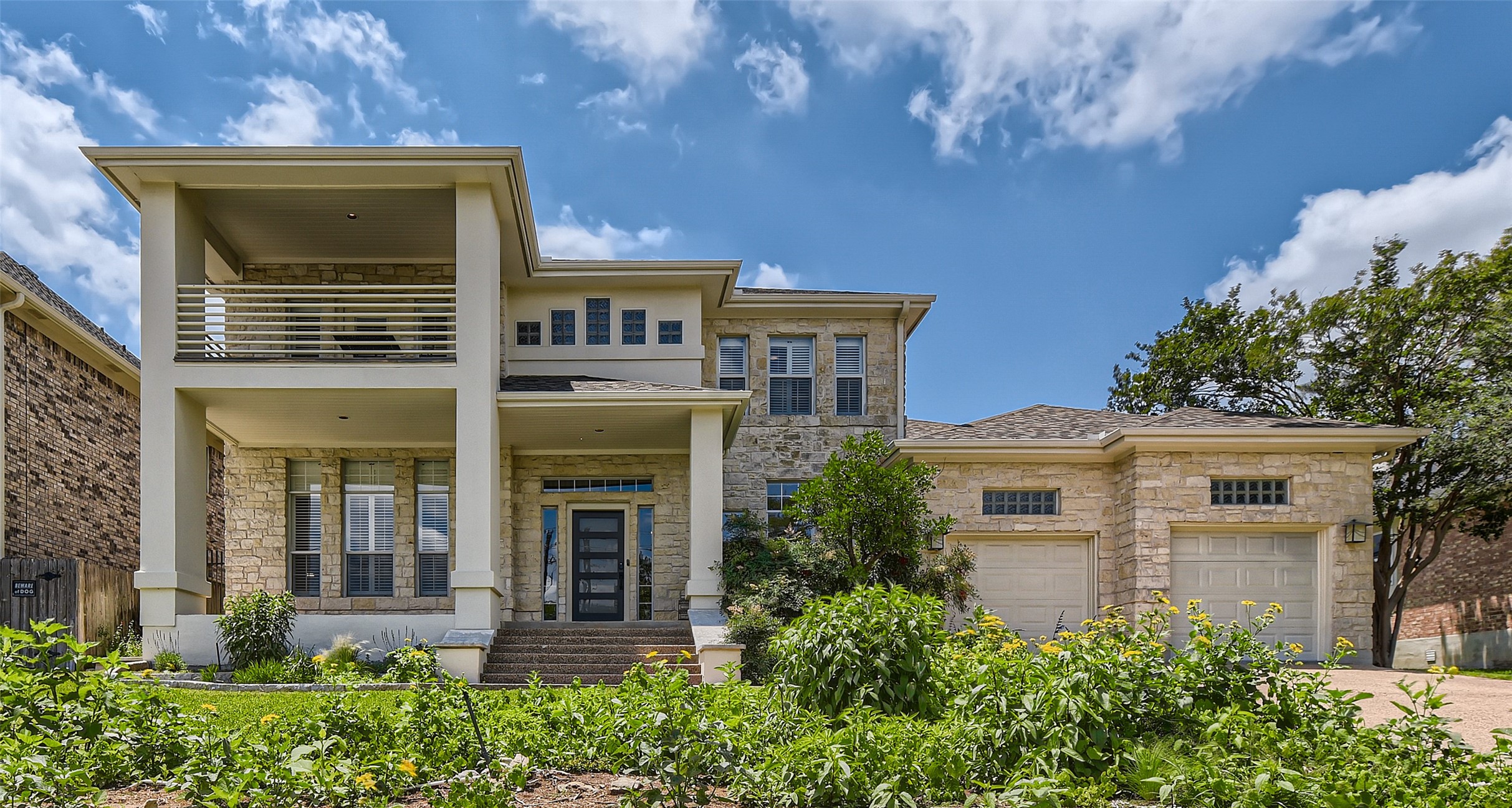 View of front of property with a garage, stone siding, concrete driveway, and a balcony
