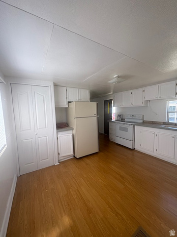1111 North 2000 West, Unit 293 Farr West, UT 84404 - Photo 4 of 13 Open-concept kitchen area featuring wood-finish flooring, white cabinetry, a built-in oven range, and a built-in refrigerator