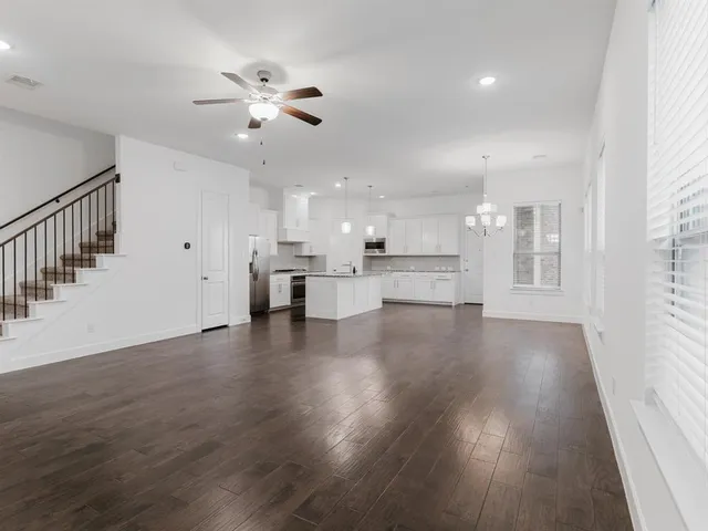 a view of an empty room and kitchen with wooden floor and a window