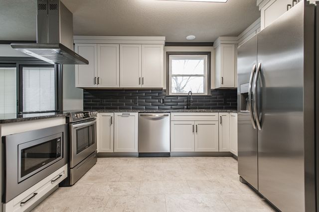 a white kitchen with stainless steel appliances granite countertop a stove a sink and a refrigerator