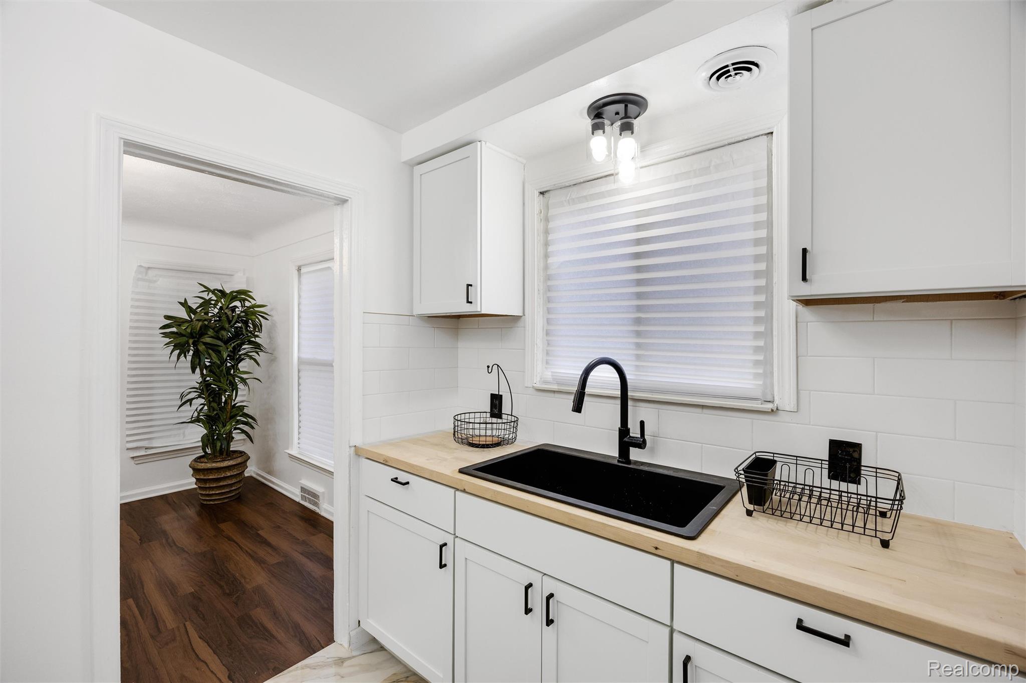 11566 Nottingham Road Detroit, MI 48224 - Photo 11 of 23 White shaker-style cabinetry with matte black hardware, wood-finish countertops, black undermount sink with a matte black gooseneck faucet, white subway tile backsplash, and wood-finish flooring