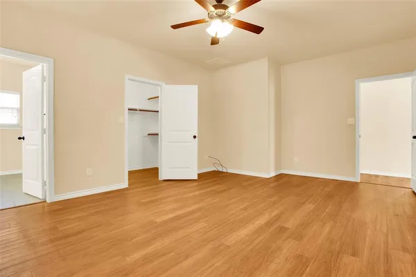 a view of an empty room with wooden floor and a ceiling fan