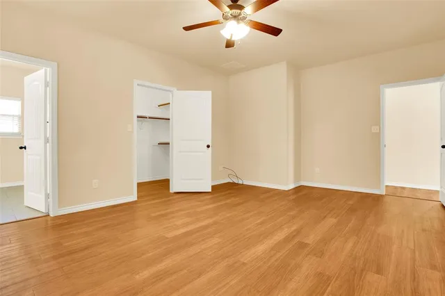 a view of an empty room with wooden floor and a ceiling fan