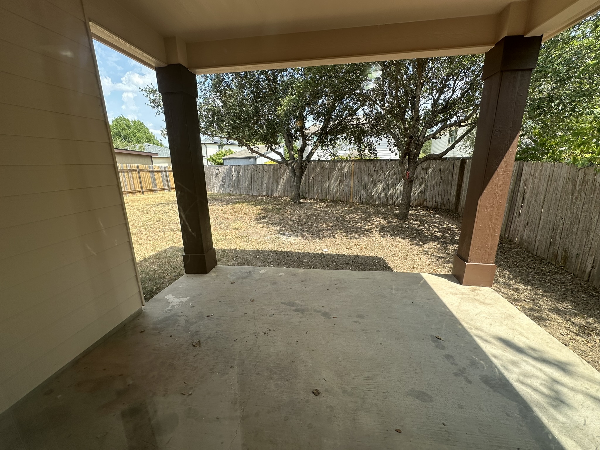 4507 Peach Grove Road Austin, TX 78744 - Photo 35 of 35 A covered concrete patio overlooks the fenced backyard shaded by mature trees.