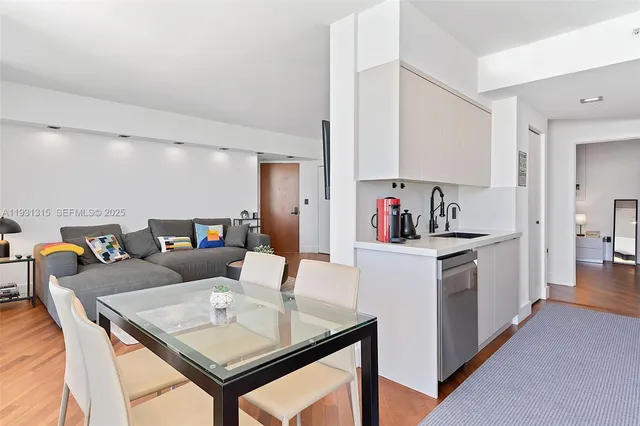 a living room with stainless steel appliances furniture a rug and a kitchen view