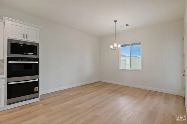 a view of an empty room with wooden floor and a kitchen