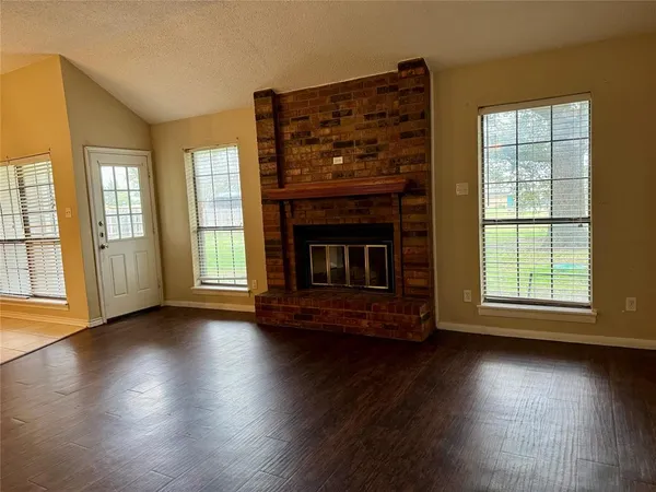 an empty room with wooden floor fireplace and windows