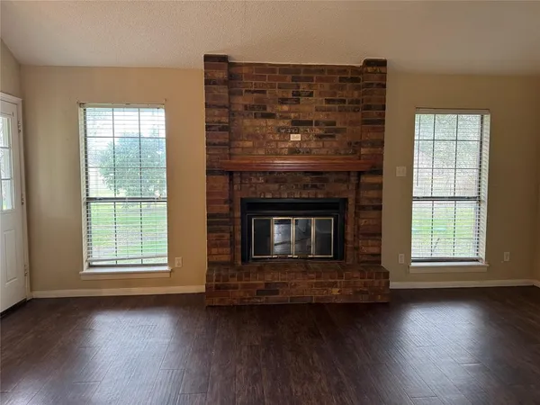 an empty room with wooden floor fireplace and windows