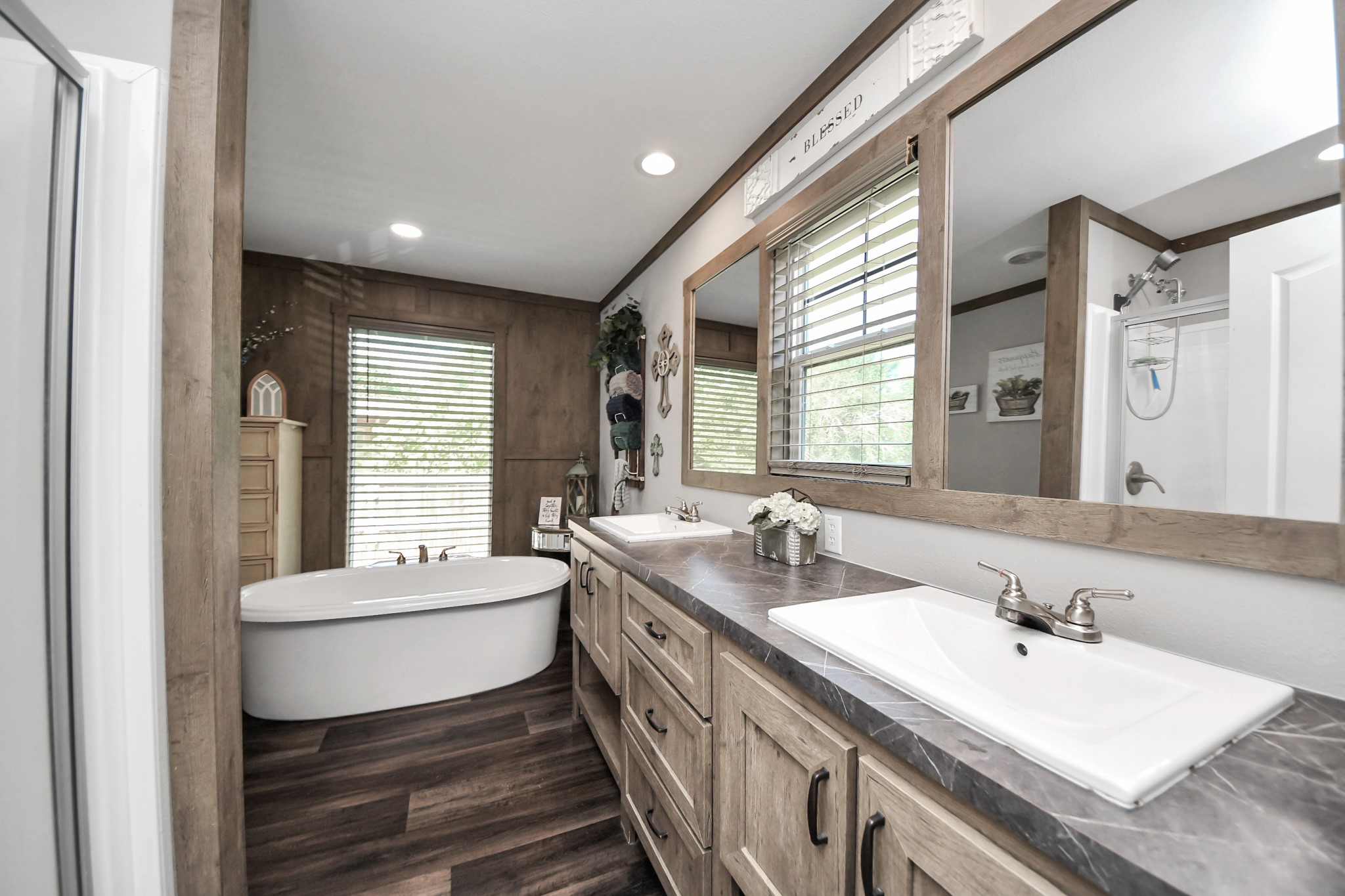 131 Kiowa Court Rosharon, TX 77583 - Photo 19 of 42 This bathroom features a modern, rustic design with a freestanding bathtub, dual sinks, and a large mirror. The wood accents and natural light create a warm, inviting atmosphere. Ideal for relaxation and functionality.