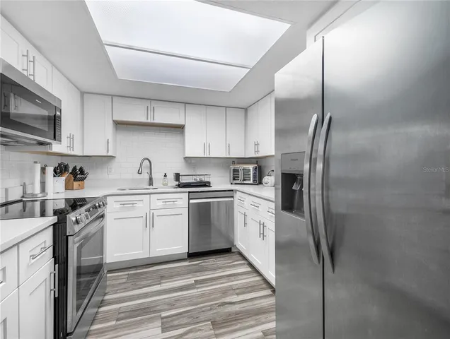 a kitchen with stainless steel appliances granite countertop a refrigerator a stove and a sink with wooden floor