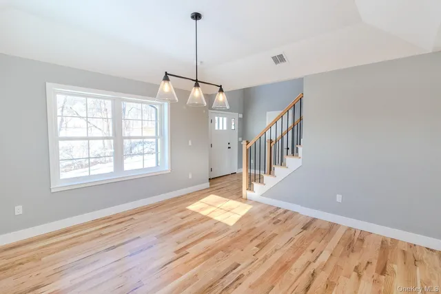 a view of an empty room with wooden floor fridge and a window